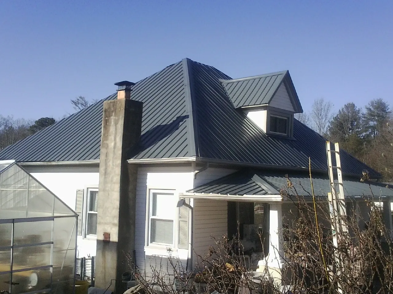 Dark blue standing seam metal roof on a white farmhouse with dormer — Slate & Tile Roof Repair by Roofing Brothers in Neville