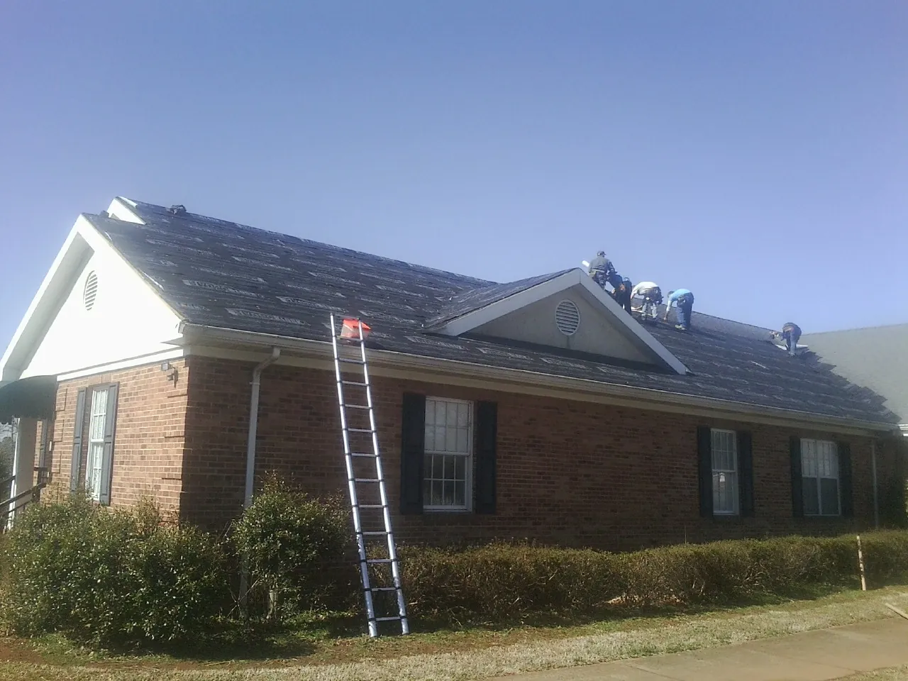 Crew tearing shingles off a brick ranch roof with a ladder set — Emergency Roof Repair work by our crew in Neville