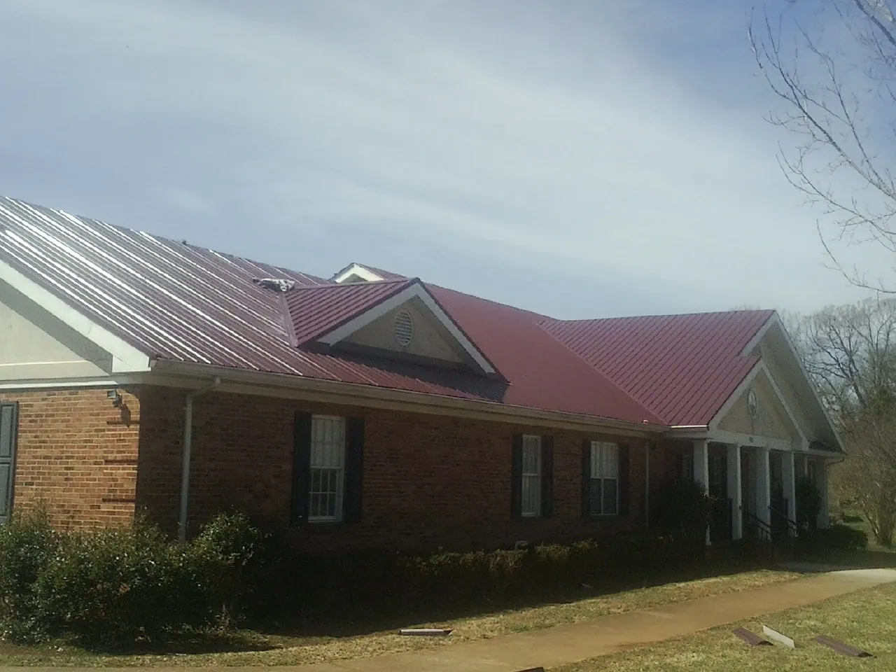 Red metal roof with gabled entries on a long brick building, from a Hail Damage Roof Repair job in Neville
