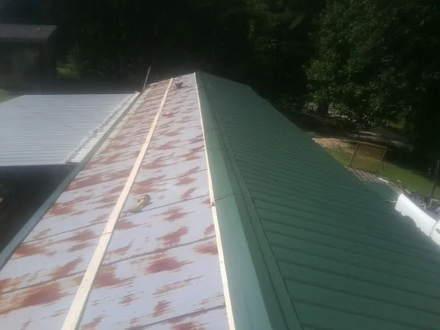 Old rusted panels beside newly installed green metal roofing — Wind Damage Roof Repair by Roofing Brothers in Neville