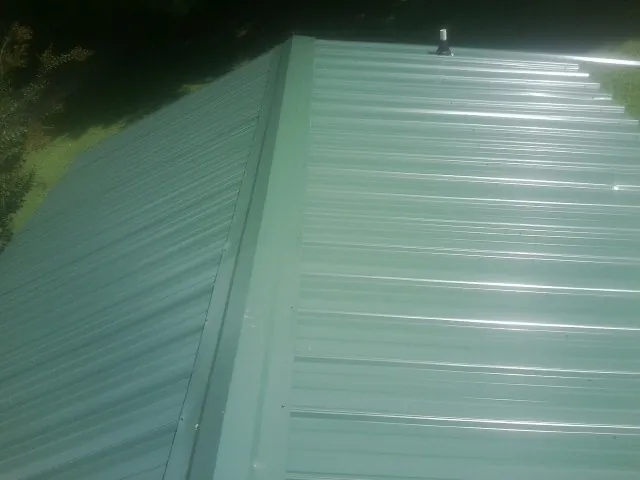 New green metal panels meeting at the ridge of a roof — Flat Roof Repair work by our crew in Neville