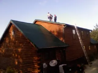 Crew on the ridge of a green metal roof on a two story log home in Neville