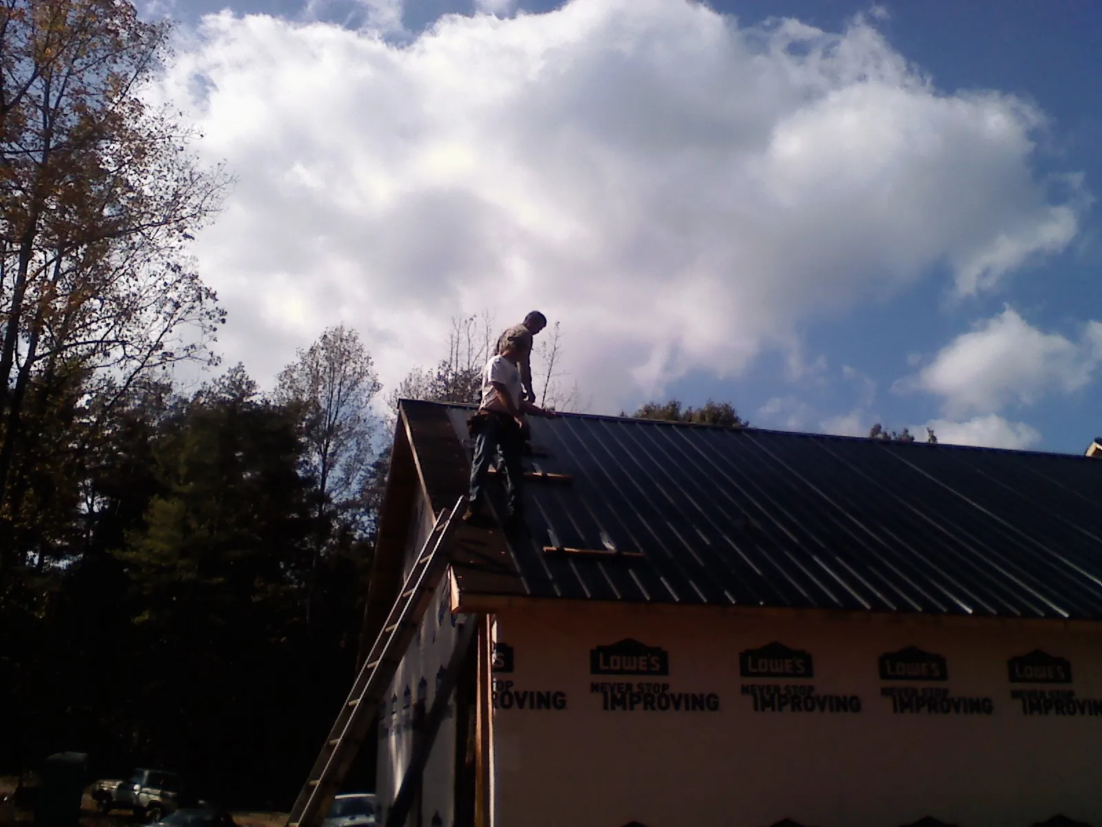 Roofer fastening dark metal panels high against a cloudy sky, from a Roof Inspection job in Neville