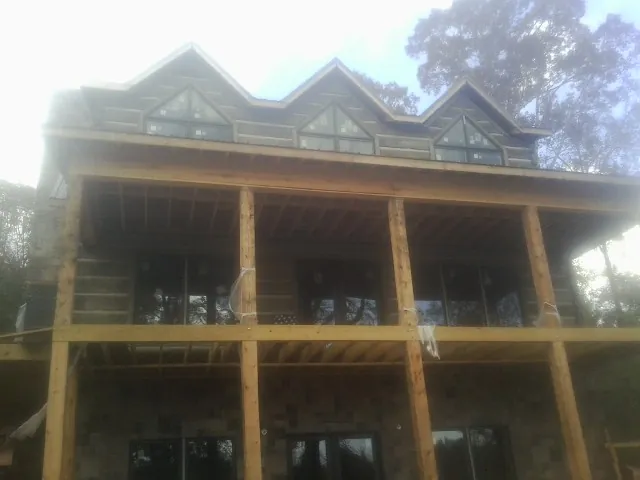 Dormers and porch framing on a large log home under construction — Roof Coating work by our crew in Neville