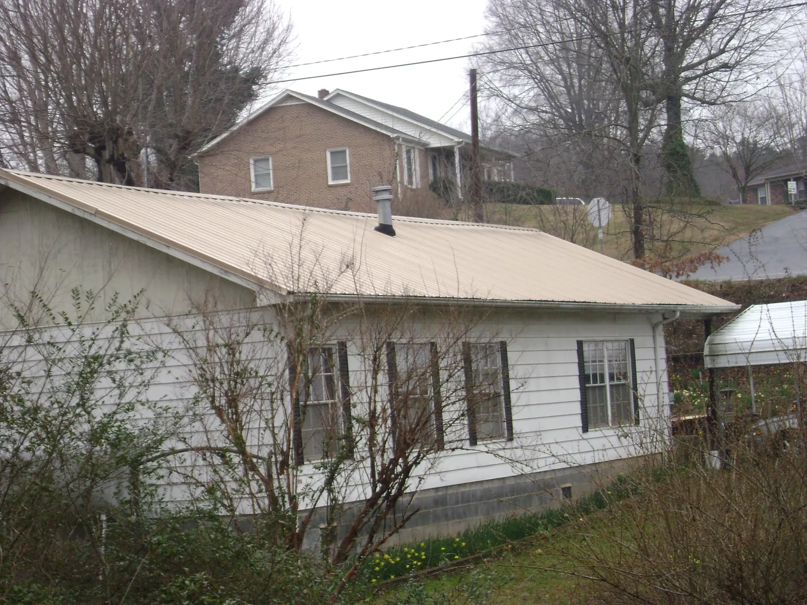 Tan metal roof on a white sided house set into a hillside — Commercial Roofing by Roofing Brothers in Neville