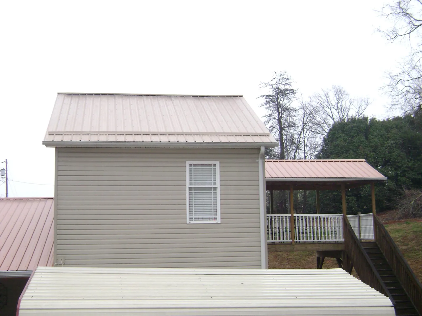 Tan metal roofs on a two story addition and attached porch, from a Roof Replacement job in Neville
